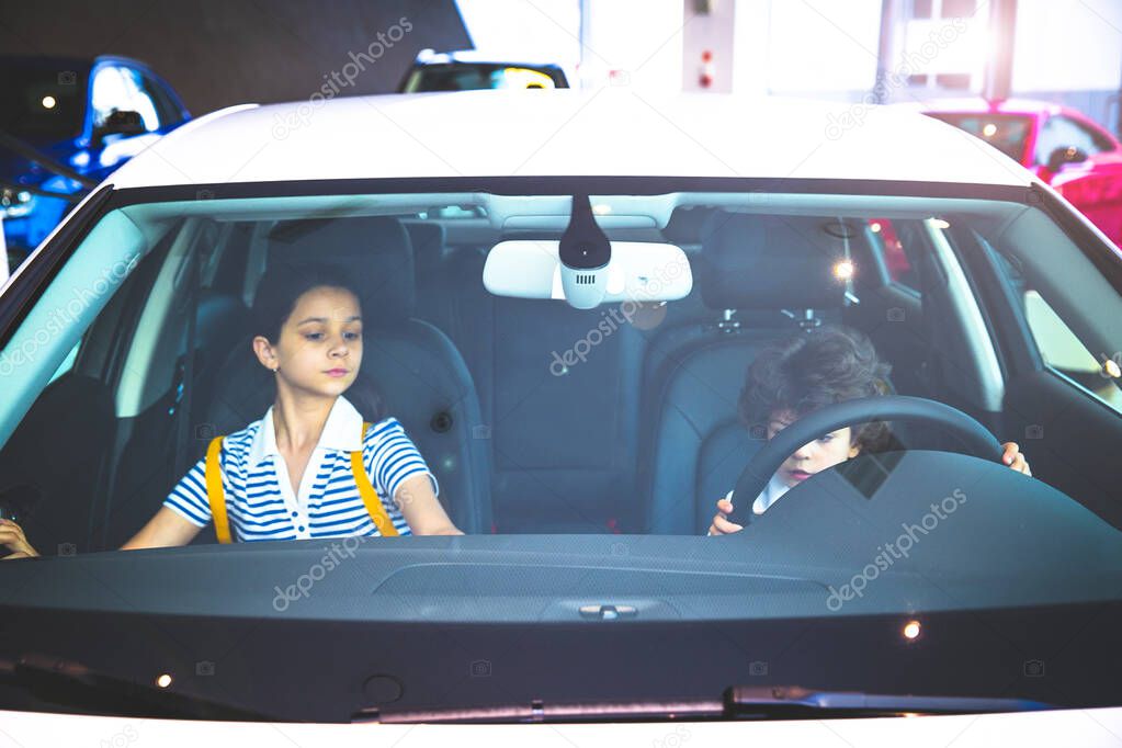 Children observing and testing new car in dealership. Little boy sitting in driver's seat, car cabin. Little boy holding hands on steering wheel, smiling. front view. Selective focus. Light blur.