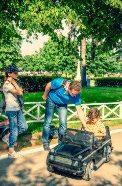 Sarı tişörtlü sevimli 4 yaşındaki çocuk parkta siyah elektrikli bir araba sürüyor. Ailesi yazın lunaparkta.
