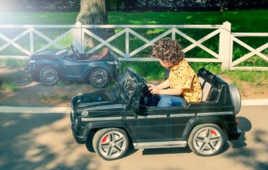 Sarı tişörtlü 4 yaşındaki tatlı çocuk parkta siyah elektrikli bir araba sürüyor.