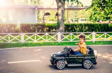 Sarı tişörtlü 4 yaşındaki tatlı çocuk parkta siyah elektrikli bir araba sürüyor.