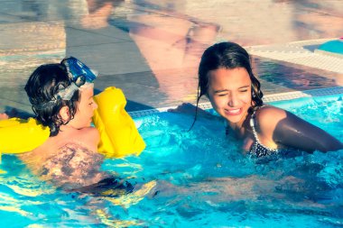 İki mutlu çocuk gündüz vakti yüzme havuzunda oynuyorlar.