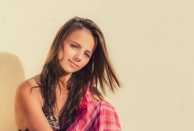 Parlak bikinili güzel kız duvarın yanında oturuyor. Modaya uygun bir tatil yeri. Boşluğu kopyala