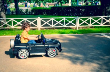 Sarı tişörtlü 4 yaşındaki tatlı çocuk parkta siyah elektrikli bir araba sürüyor.