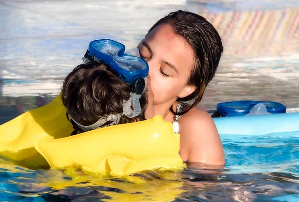 Older sister hugs and kisses her little brother seated in the pool