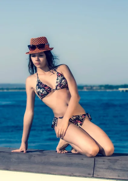 海の上で水着の若い美しい女の子 頭の上の帽子 海の上の桟橋にグラマラスなポーズ — ストック写真