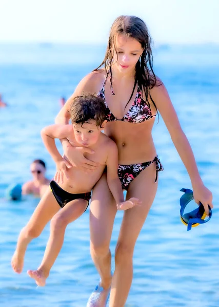 Denizden gelen genç kız kardeşini kıyıya taşıyor.