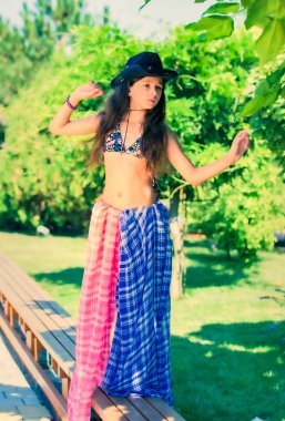 Plaj kovboyu şapkalı, mayo giymiş, gülümseyen ve tropik yeşile karşı poz veren uzun saçlı güzel bir esmer.