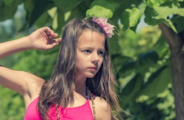 Yeşil çimenlerin ve ormanın arka planında poz veren pembe başlıklı manken görünümlü bir kız..