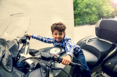 Şehir caddesinde büyük siyah motosikletli şirin küçük bir çocuk.