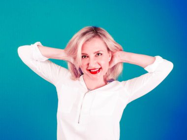 Mutlu, olgun, sarışın kadın ellerini başının arkasına koyup sırtını yaslıyor ve gülümseyerek kameraya bakıyor.