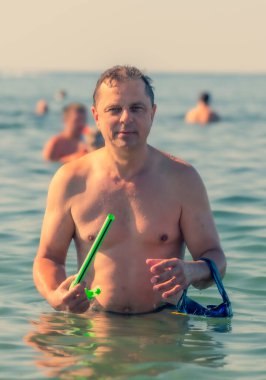 Yüzme maskeli ve şnorkelli gülümseyen olgun bir adam kameraya bakıyor. Babam deniz kıyısında.