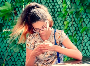 Akıllı telefona bakan bir kız. Genç Avrupalı bir kız bir kafede bankta oturuyor ve telefonu kullanıyor..