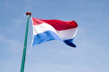  Hollanda bayrağı bayrak direği üzerinde mavi gökyüzü arka plan üzerinde sallayarak.