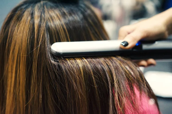 Hairdresser using hair straightener on brown-haired woman