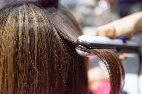 Hairdresser using hair straightener on brown-haired woman