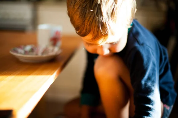 A boy sitting at home in the light looking down