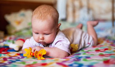 Bir yatakta evde bir gelişimsel oyuncakla oynayan bebek