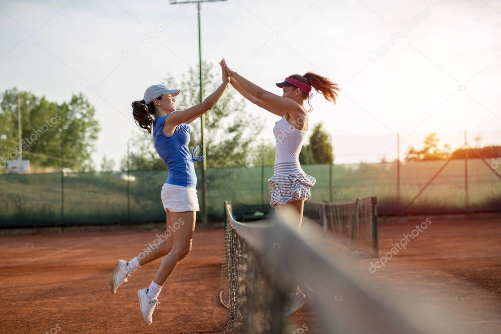 Beautiful happy girls smiling after playing tennis high five outside