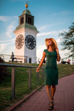 Süre yeşil bir elbise içinde gülümseyen gün batımına doğru yürüyen güzel genç kadın