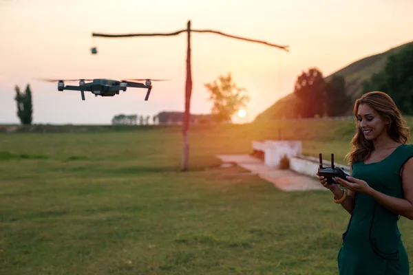 Beautiful young woman flying a drone at sunset while smiling