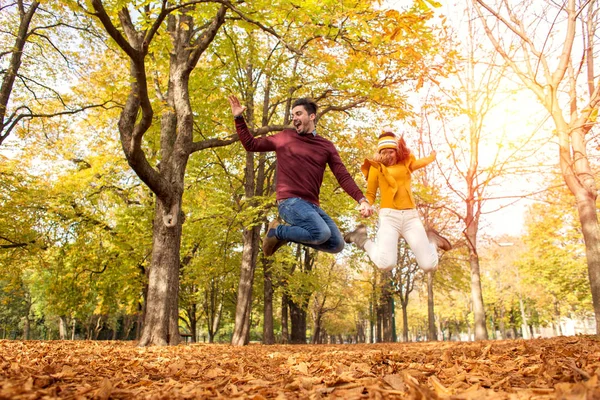 幸せなカップルは 秋に公園でジャンプと笑みを浮かべて — ストック写真