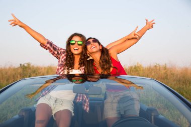 İki güzel genç kadın gülümseyerek ve eller havada atma sırasında bir Cabrio araba gezintiye zevk