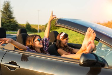 Gün batımında gülümseyen iki güzel genç kadın bir araba zevk üstü açık bir arabayla binmek