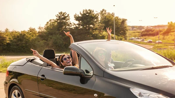 Two young beautiful girls driving in a convertible with hands outside