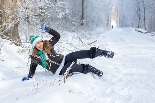 Beautiful young woman falling down on icy road in the forest daytime