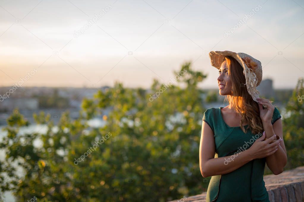 Beautiful young woman with a hat smiling at the sunset in a green dress