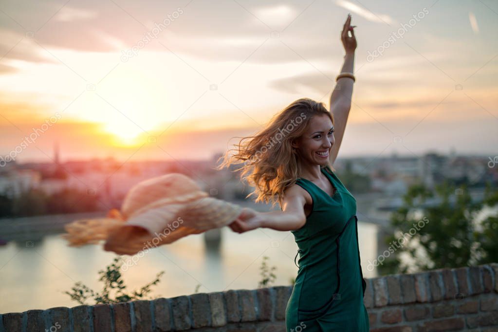 Beautiful young woman playing with her hat at sunset while smiling and turning