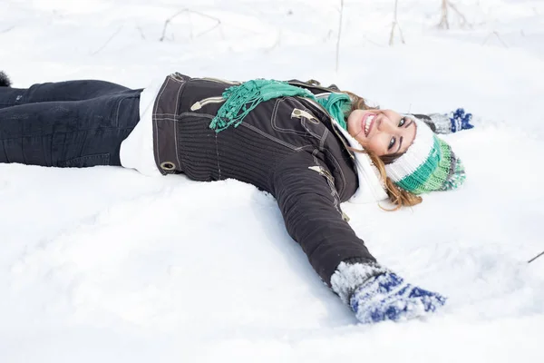 Beautiful young woman laying in the snow making a snow angel while smiling