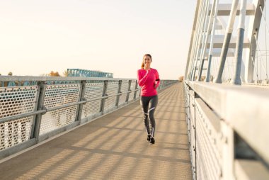 Güzel genç gülümseyen süre onun egzersiz yapıyor bir köprü üzerinde çalışan kadın yerleştirmek