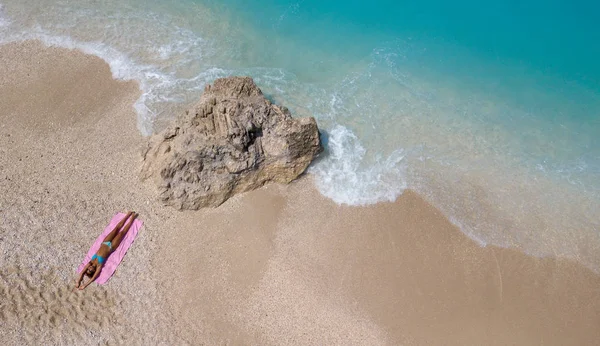 Beautiful young woman sun tanning on a beach by the water photographed from above