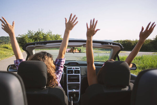 Two beautiful young women driving in a convertible with hands in