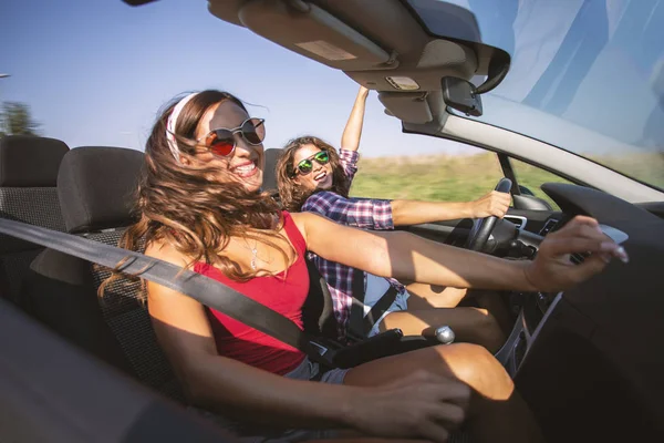 Dos chicas hermosas jóvenes conduciendo en un convertible mientras bailan — Foto de Stock