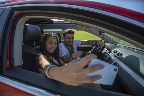 Feliz hermosa pareja joven tomando una selfie en un coche — Foto de Stock