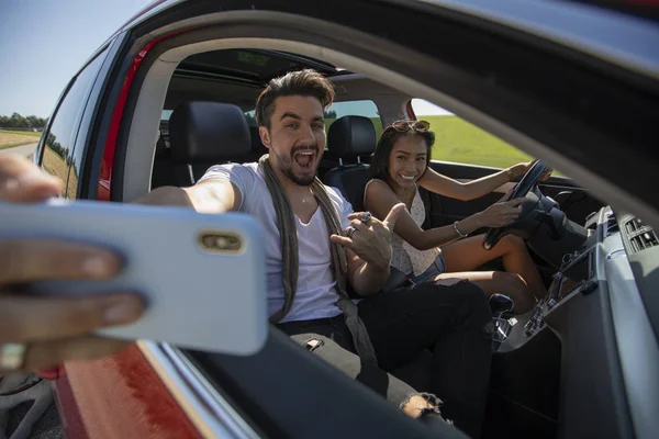 Feliz hermosa pareja joven tomando una selfie en un coche — Foto de Stock