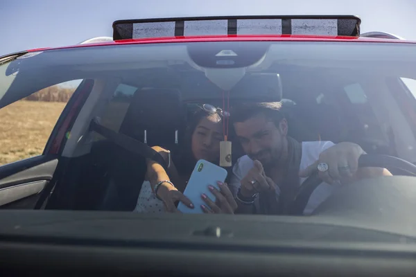 Feliz hermosa pareja joven tomando una selfie en un coche — Foto de Stock