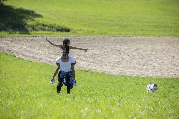 Счастливая молодая пара, идущая по полю травы и играющая — стоковое фото