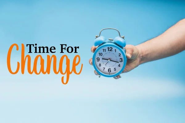 Time for Change and a Hand Holding a blue Analog Alarm Clock