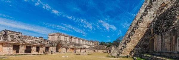 UXMAL, MEXICO - FEB 28, 2016: Tourists between the Nun\'s Quadrangle (Cuadrangulo de las Monjas) building complex and the Pyramid of the Magician (Piramide del adivino) at the ruins of the ancient Mayan city Uxmal, Mexico