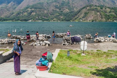 SANTIAGO ATITLAN, GUATEMALA - MARCH 24, 2016: Local indigenous women wash laundry in Atitlaan lake in Santiago Atitlan village. clipart