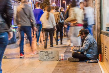Madrid, İspanya - 22 Ekim 2017 Calle Gran Via caddesinde yürüyen insanlar evsiz bir adamın yanından geçiyor. Tabelada 