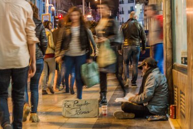 Madrid, İspanya - 22 Ekim 2017 Calle Gran Via caddesinde yürüyen insanlar evsiz bir adamın yanından geçiyor. Tabelada 