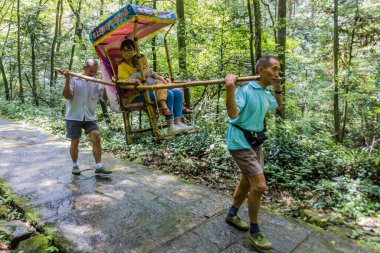 ZHANGJIAJIE, ÇİN - 8 AĞUSTOS 2018: Çin 'in Hunan ilindeki Zhangjiajie Ulusal Orman Parkı' ndan bir ziyaretçiyle birlikte bir tahtırevan taşıyıcıları