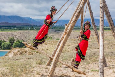 ISSYK KUL, KYRGYZSTAN - JULY 15, 2018: Local girls at a swing at the Ethnofestival Teskey Jeek at the coast of Issyk Kul lake in Kyrgyzstan clipart