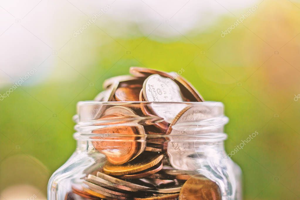 Coins in the glass jar against blurred green natural background for save money, business and finance concept