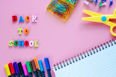 Okul malzemeleri ile defter, renkli kalem, makas, Ciltçi klibini, itme iğne ve eğitim kavramı için pembe arka plan üzerinde ahşap metin okul için