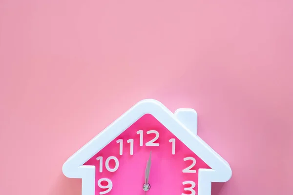 Pink clock with home shape at 12 o'clock on pink background for family time concept